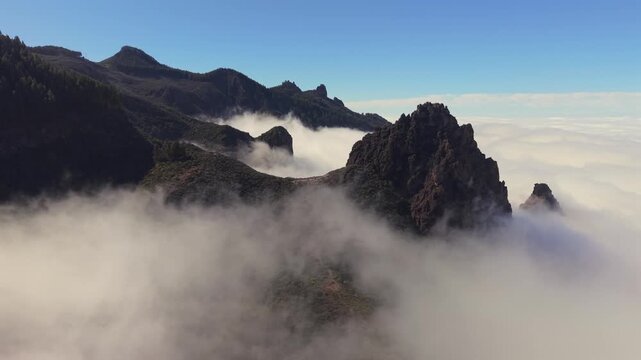 Breathtaking aerial shot revealing the majestic Roque Grande and surrounding mountain peaks rising above a dense layer of white clouds