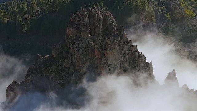 Breathtaking aerial shot of the majestic Roque Grande emerging from a sea of clouds. A volcanic rock formation surrounded by mist
