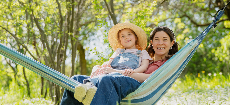 Happy Mother's Day concept with beautiful woman and little daughter embracing in garden hammock