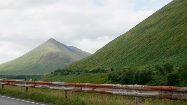 Beautiful landscape of green mountains and valleys in the scottish highlands seen from a moving car on a scenic road with a rusty guardrail