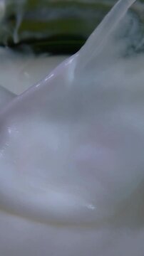 Close up of white cream being stirred using a transparent spoon. Smooth mixing texture, skincare or cosmetic product preparation concept.