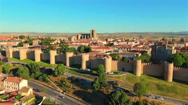 A drone descends toward the fortified walls of Avila, Spain, revealing rooftops and a busy road below.