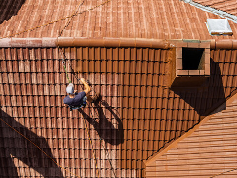 Roof renovation process with spray painting of roof tiles, including priming and applying second coat of paint on a residential roof, showing professional exterior maintenance and refurbishment work
