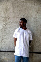 Fototapeta premium Man in white t-shirt and jeans stands against a textured wall.