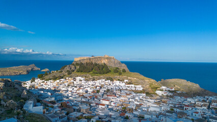 Obraz premium Panoramic view of the historical white houses in Lindos village with the Acropolis on the cliff and deep blue sea on Rhodes island Greece