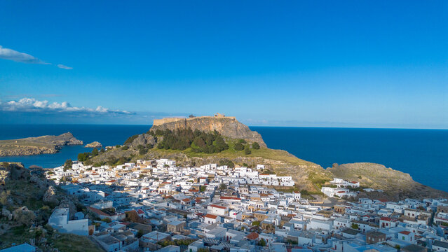 Panoramic view of the historical white houses in Lindos village with the Acropolis on the cliff and deep blue sea on Rhodes island Greece