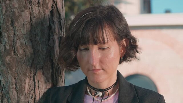 Female artist reviewing sketches in notebook outdoors near a tree during creative process