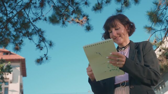 Female artist drawing in sketchbook outdoors in a summer park