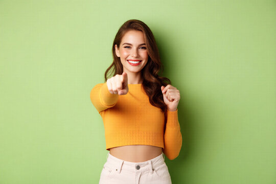 Cheerful Young Woman Pointing Finger Forward with Bright Smile and Confident Gesture