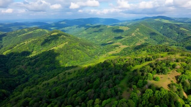 Aerial view of lush green rolling hills and dense forests under a partly cloudy sky