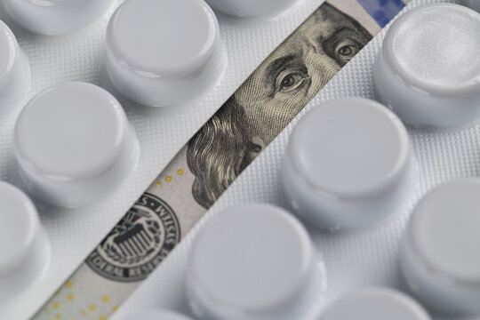 Benjamin Franklin portrait on 100 dollar bill visible between medicine blister packs