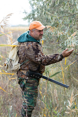 Fototapeta premium A hunter with a gun in camouflage clothing. A senior man with a gun, medium shot, searching for game.