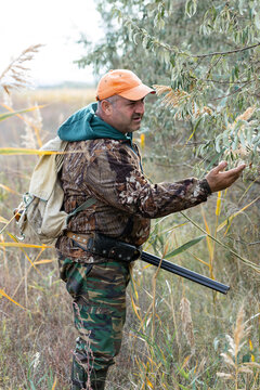 A hunter with a gun in camouflage clothing. A senior man with a gun, medium shot, searching for game.