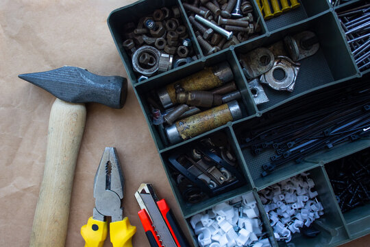 Hand tools and organizer box with screws and bolts flat lay. Top view of hammer, pliers, utility knife and plastic hardware storage case on craft paper. Home repair, workshop and DIY concept.