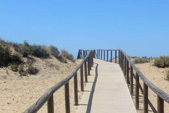 Wooden walkway leading to a sunny beach, surrounded by dunes and coastal scenery