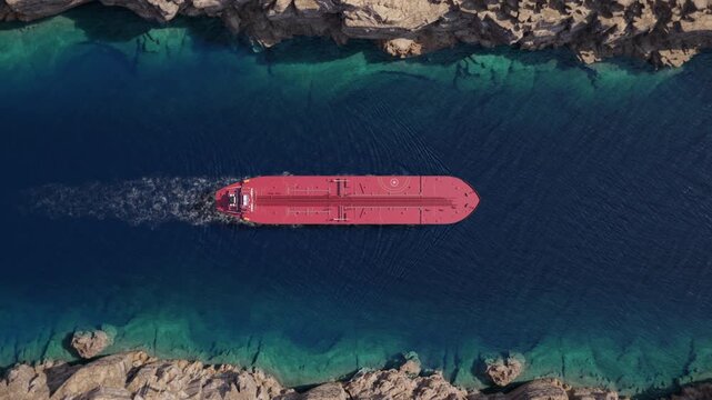 Top down view of oil tanker moving across narrow rocky strait