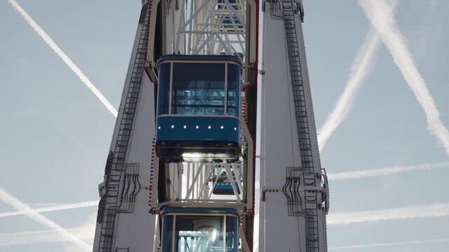 Close-up frontal view of enclosed passenger cabins moving between the white structural supports of a large observation wheel