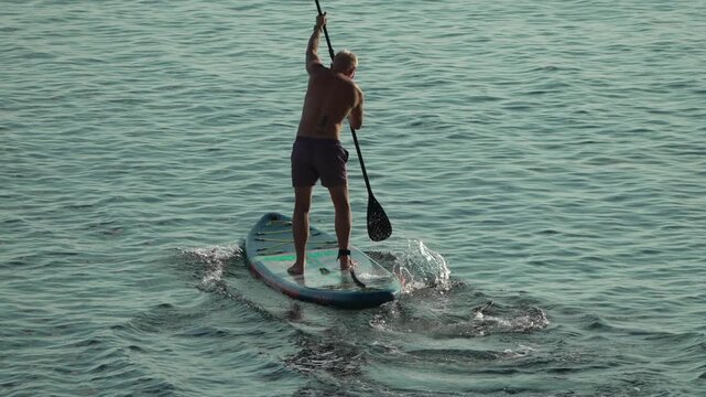Paddleboarding man enjoys active leisure on the calm ocean water during a sunny summer day