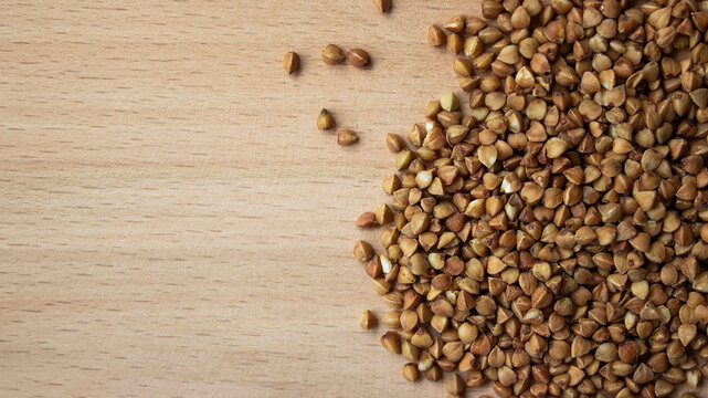 Raw buckwheat groats on wooden cutting board background. Pile of dry organic buckwheat seeds on wooden texture, high angle flat lay view with negative copy space for text.