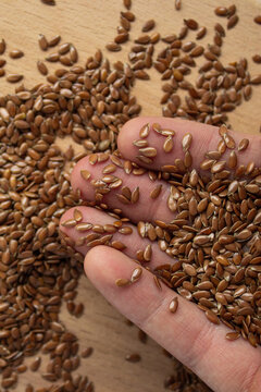 Flax seeds in farmer hand close up. Heap of raw organic linseed held by human hand on wooden background. Healthy superfood ingredient, agriculture harvest and dietary supplement concept