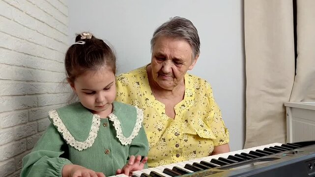 Elderly grandmother teaching little sweet girl playing piano, smiling with happiness, staying at cozy home, spending time together. Family, Love, Education Concept.