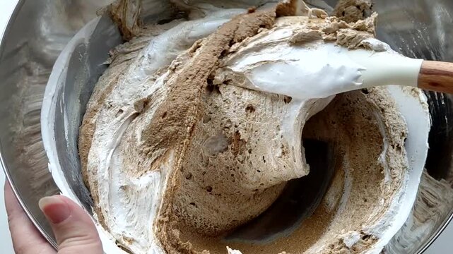 A person kneads the halva ingredients in a bowl with a spatula, preparing it. Various ingredients are visible in the finished mixture. Sunflower halva.
