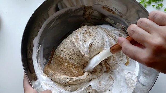 A person kneads the halva ingredients in a bowl with a spatula, preparing it. Various ingredients are visible in the finished mixture. Sunflower halva.