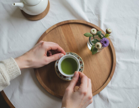 Top View Flat Lay of Hands Holding Small Cup of Japanese Green Tea Matcha on Wooden Tray