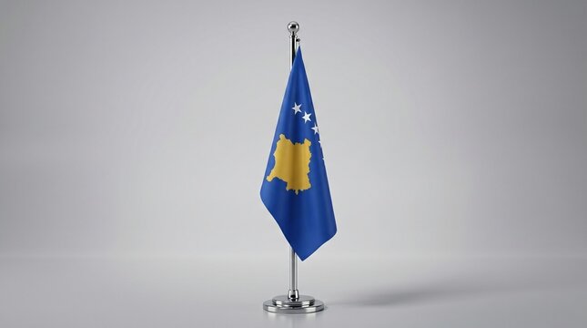 A small table flag of Kosovo, featuring its blue field with a gold map and six white stars, displayed on a silver stand against a plain background.