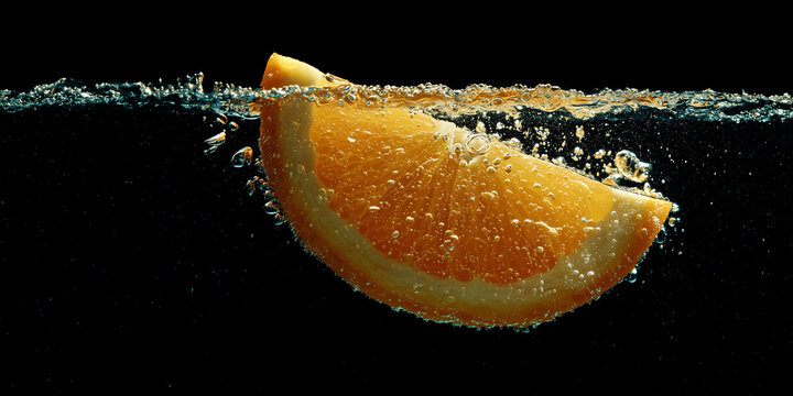 A slice of orange falling into the water with bubbles and splashes