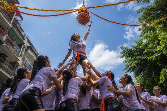 Women Govinda Team Stretching to Reach Dahi Handi Pot During Janmashtami Festival Celebration Under Blue Sky in India