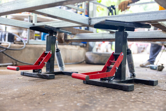 Adjustable metal car jack stands supporting vehicle frame in garage workshop with tools and mechanic hands nearby, practical and industrial scene conveying focused work and safety