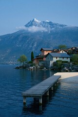 Fototapeta premium Tranquil lakeside village with wooden dock and snowcapped mountain backdrop for serene wallpaper and banner design