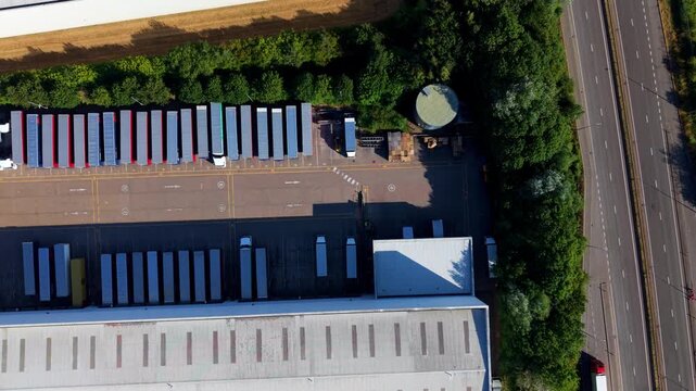 Overhead top-down drone video footage capturing symmetrical rows of heavy goods vehicle (HGV) semi-trailers docked in loading bays at a commercial distribution warehouse