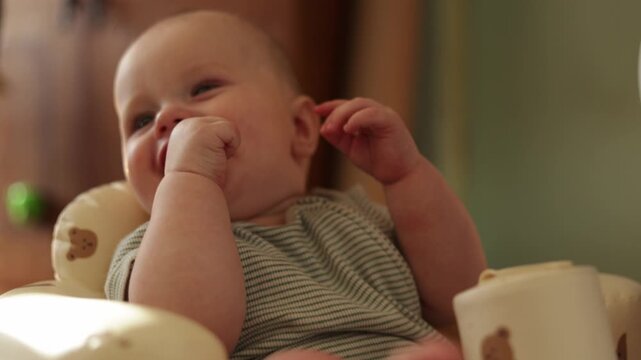 Adorable baby in high chair exploring fingers and looking around curiously