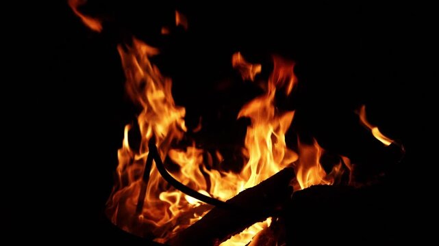 Close-up of vibrant orange flames dancing on burning logs in darkness