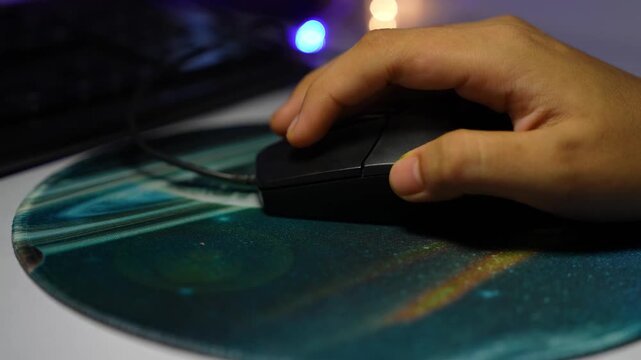 Close-up of a hand using a computer mouse on a mouse pad with soft colored lights in the background