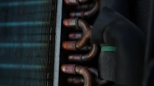Copper pipes and metal fins inside an air conditioner or cooling unit, showing industrial parts texture and mechanical detail in low light
