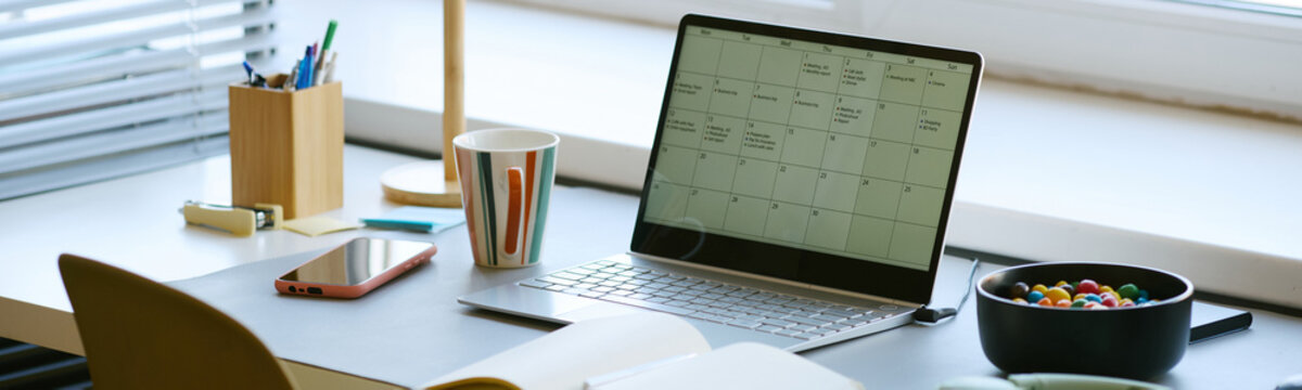 Wide shot of laptop displaying calendar on desk beside smartphone and notebook, supporting schedule planning and task management. Ideal for productivity, remote work, time management marketing