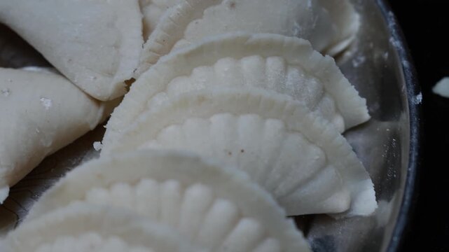 Close-up of white Puli pitha arranged in a metal tray, showing folded edges soft dough texture and a simple homemade food presentation