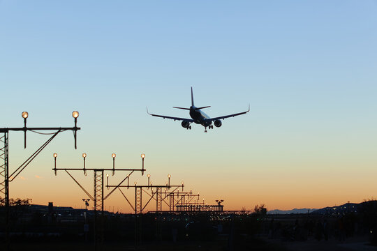 Airplane approaching runway for landing with lit guide lights at sunset