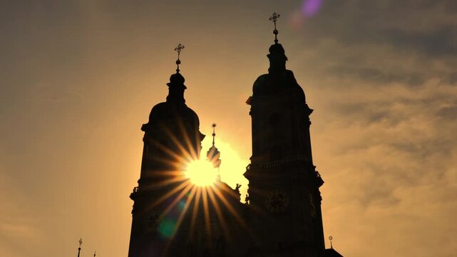 Abbey of Saint Gall with Clock Tower and Sunbeam in Backlit Against Orange Sky in Sunset in City of St Gallen, St Gallen Canton, Switzerland.