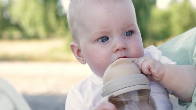 Close-up of a baby with blue eyes drinking from a bottle outdoors