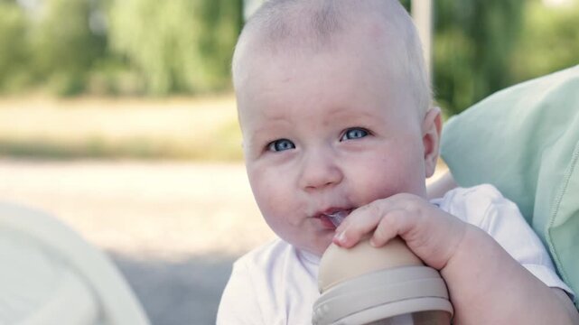 Close-up of a baby's face as they drink from a bottle outdoors