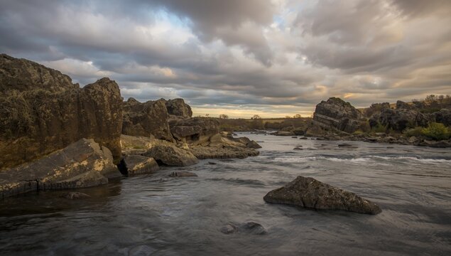 Tranquil riverside featuring rocky banks and a brooding sky with gentle water flow
