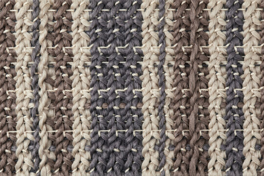 Close up of a woven fabric textile with vertical stripes in shades of gray, brown, and beige showing detailed interlaced yarn fiber structure