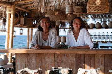 Fototapeta premium This vibrant image captures two women enjoying their time at a beachside bar, showcasing beautiful natural materials and exuding warmth and happiness by the water.