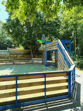 Outdoor fenced basketball court in shaded park with wooden sports structure