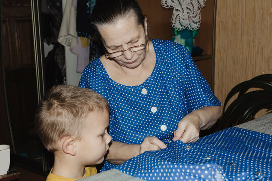 gentle grandmother blue top patiently shows her young grandson how sew piece fabric focused collaboration capturing warmth family learning passing traditions quiet joy creating something together