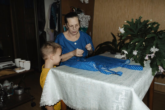 gentle grandmother blue top patiently shows her young grandson how sew piece fabric focused collaboration capturing warmth family learning passing traditions quiet joy creating something together